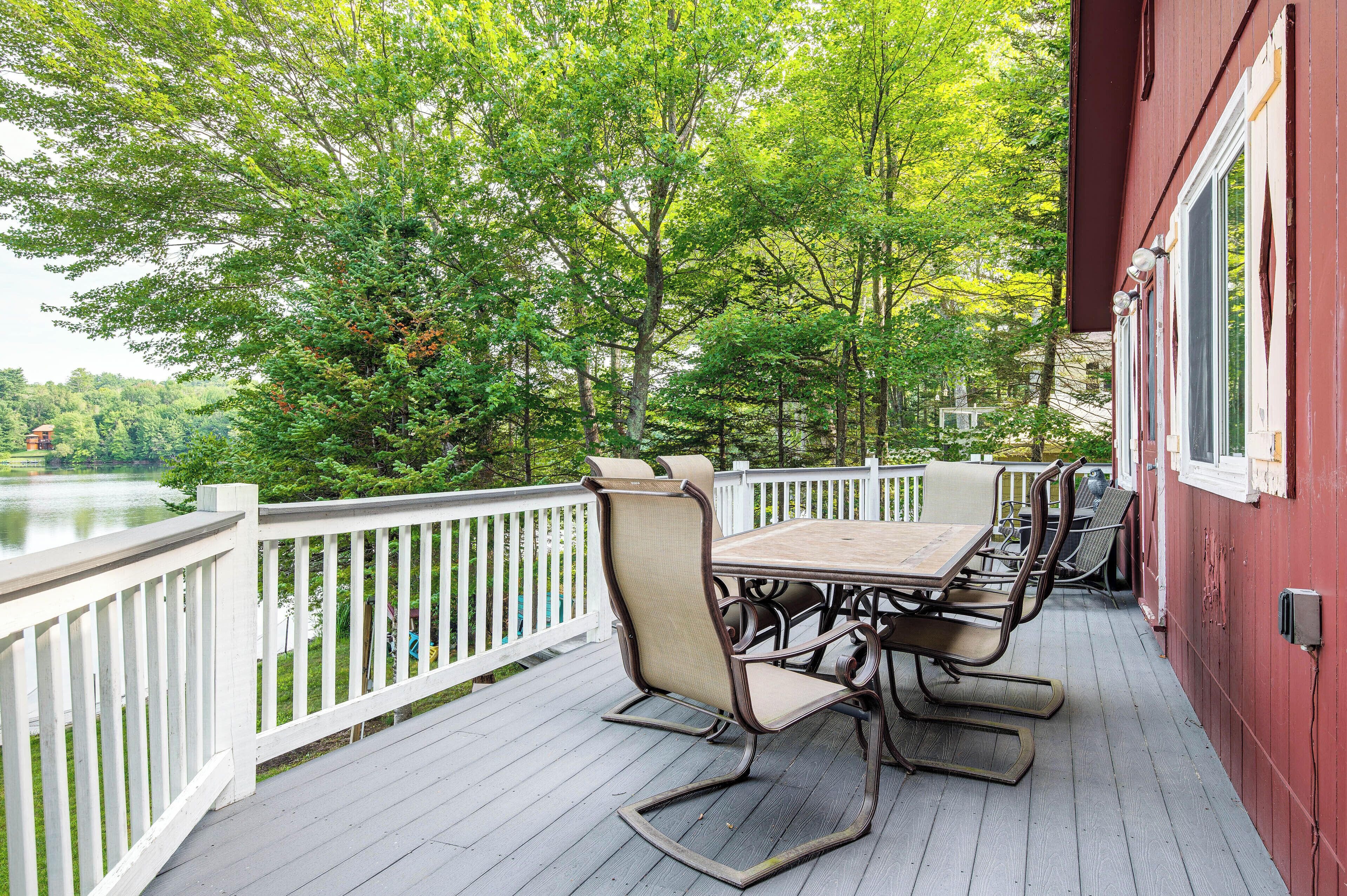 A covered outdoor deck with a table and chairs, overlooking a lake and surrounded by trees.