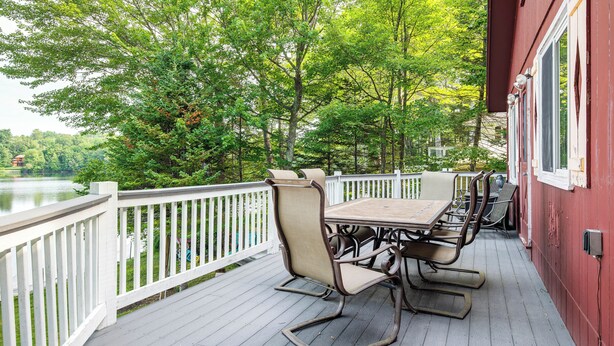 A deck with a table and chairs overlooking a lake, surrounded by trees. - Lakefront Family Home w/ Docks in Barnstead! (Center Barnstead)