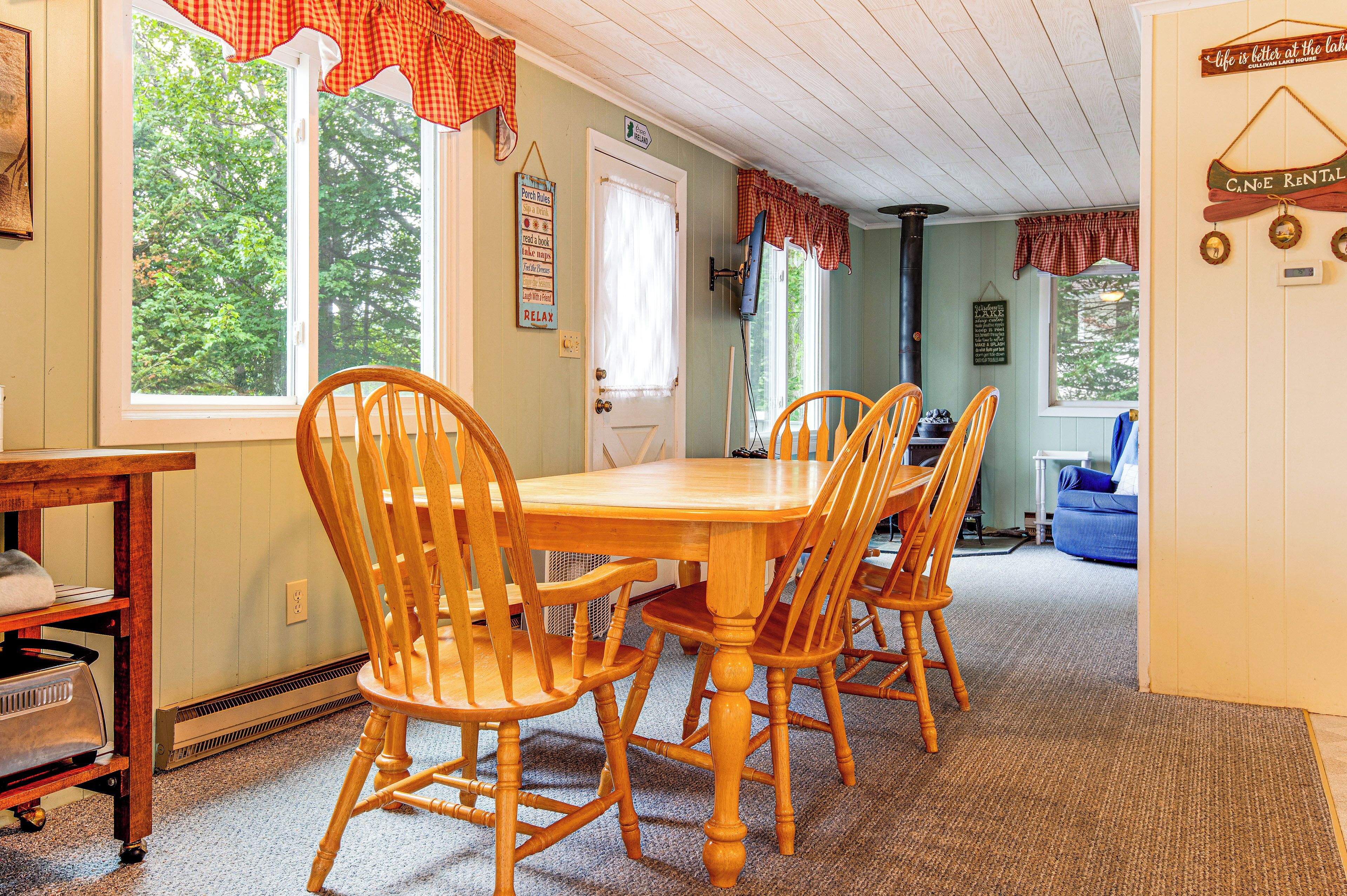 A dining area with a wooden table and chairs, a window with a view of trees, and a door with a sign.