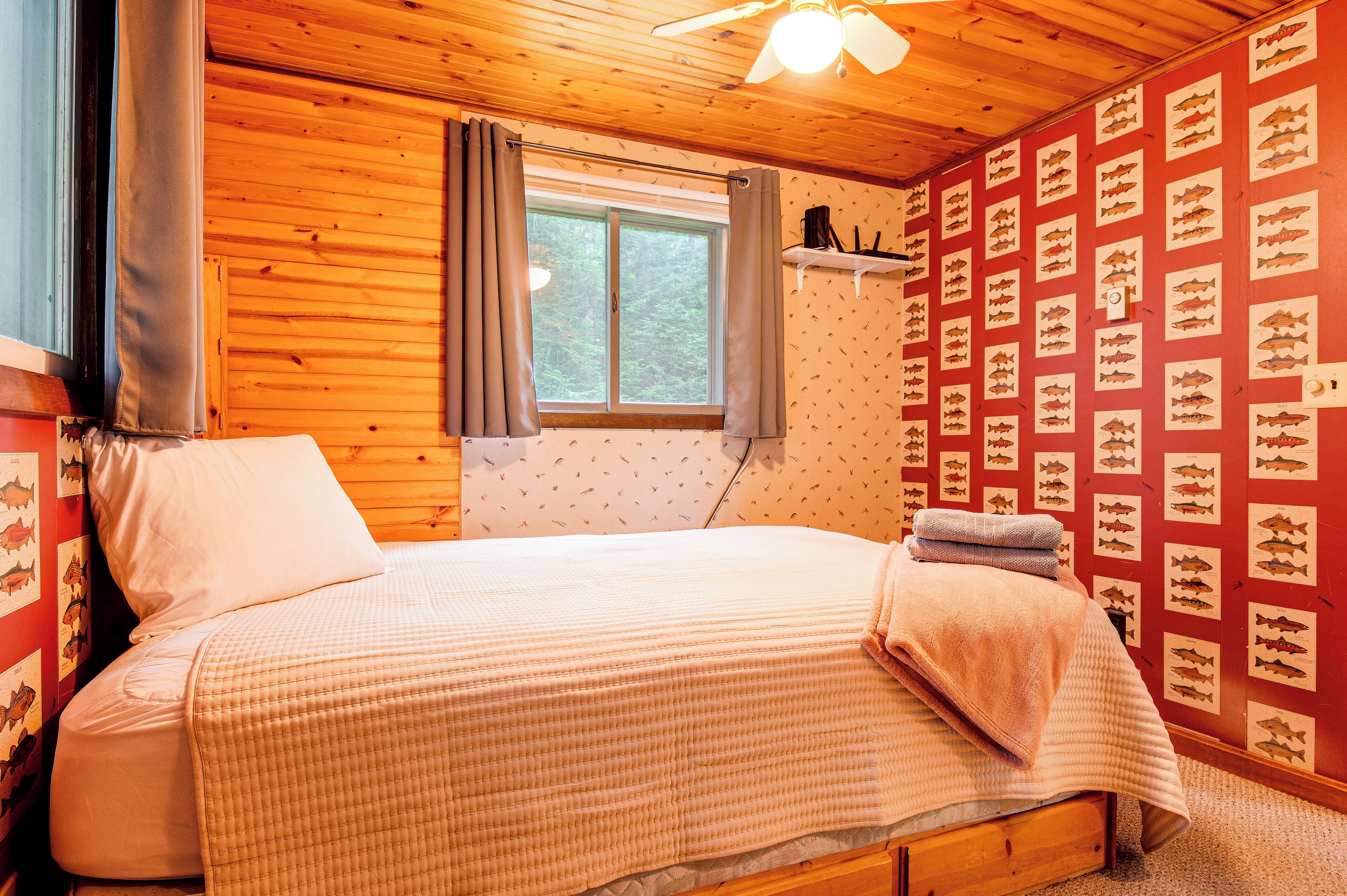 A wooden room with a bed, a window, and a wall with fish illustrations.