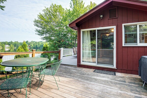 Une terrasse en bois avec une table et des chaises, une porte-fenêtre coulissante et une vue sur un lac et des arbres.