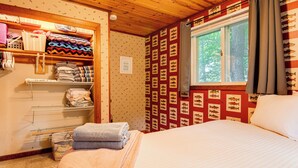 A room with a bed, a window with curtains, a wall with fish illustrations, and a shelf with folded towels. - Lakefront Family Home w/ Docks in Barnstead! (Center Barnstead)