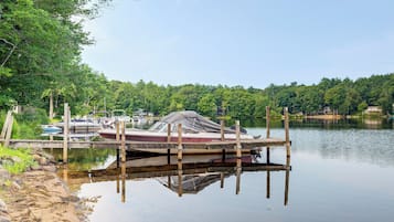 A calm lake with a dock and boats, surrounded by dense greenery and a clear sky.