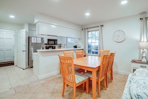 A compact kitchen with modern appliances, a dining area with wooden chairs, and a large window with blinds. - Pawleys Island Golf + Beach Getaway w/ Pool Access (Pawleys Island)