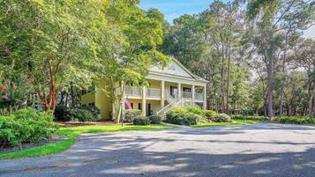 A two-story house with a porch, surrounded by lush greenery and trees.