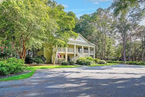 A two-story house with a porch, surrounded by lush greenery and trees. - Pawleys Island Golf + Beach Getaway w/ Pool Access (Pawleys Island)