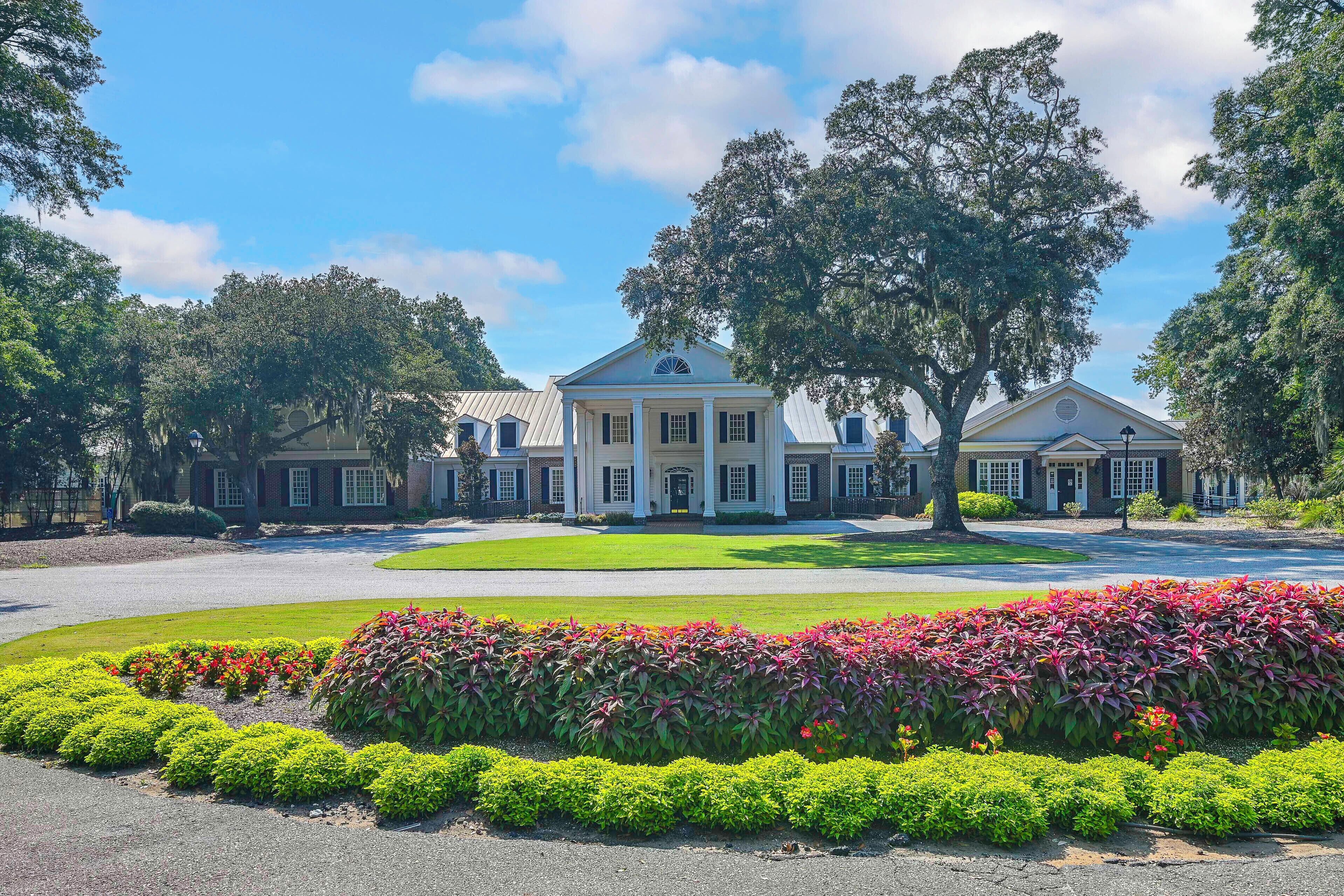 A large, two-story building with a symmetrical facade, a central entrance with columns, and a well-maintained lawn with colorful flower beds.