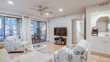 A living room with a sofa, armchairs, a coffee table, a TV, and a bookshelf.