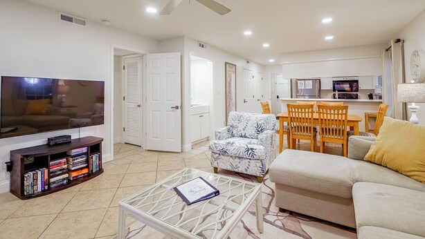 A living room with a television, books, a coffee table, a sofa, and a ceiling fan. - Pawleys Island Golf + Beach Getaway w/ Pool Access (Pawleys Island)