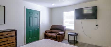 Une chambre à coucher avec un lit, une porte verte, un fauteuil en cuir marron, un téléviseur et un ventilateur de plafond.