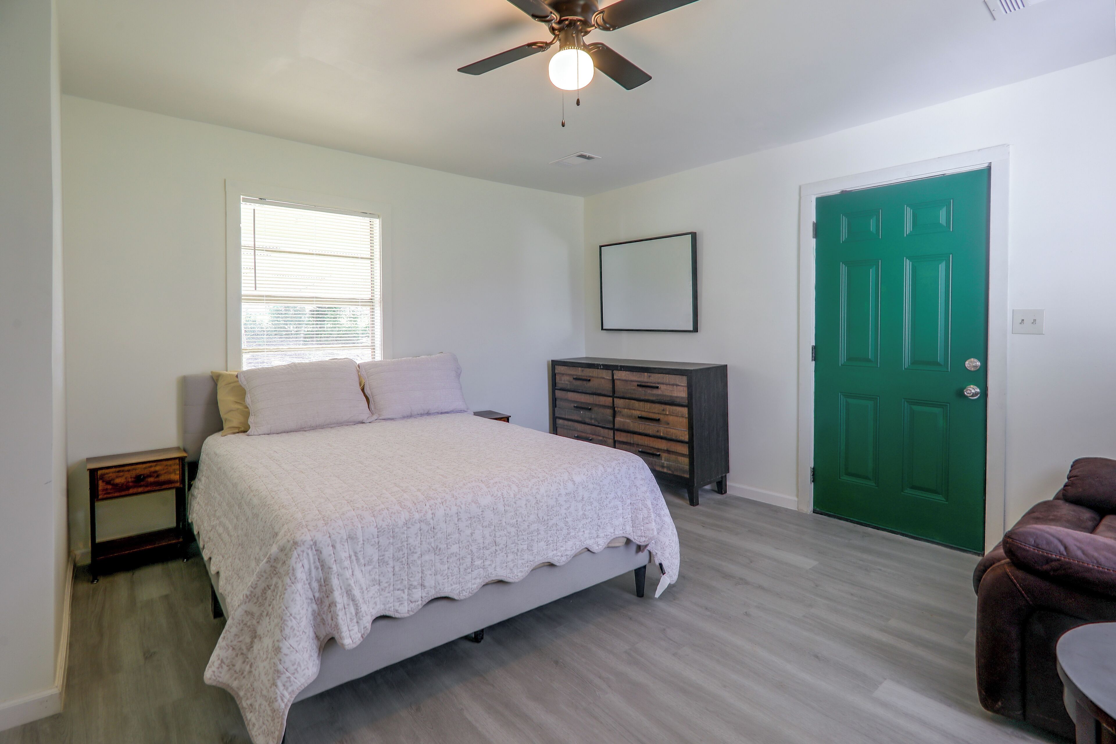 A bedroom with a bed, a dresser, a green door, and a ceiling fan.