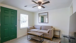 A room with a green door, a beige sofa, a small table, a ceiling fan, and a window with blinds. - Tailgate Ready! 3 Mi to Ole Miss & the Square (Oxford)