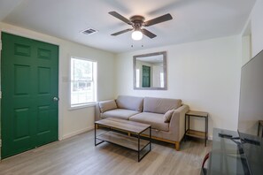 A room with a green door, a beige sofa, a small table, a ceiling fan, and a window with blinds. - Tailgate Ready! 3 Mi to Ole Miss & the Square (Oxford)