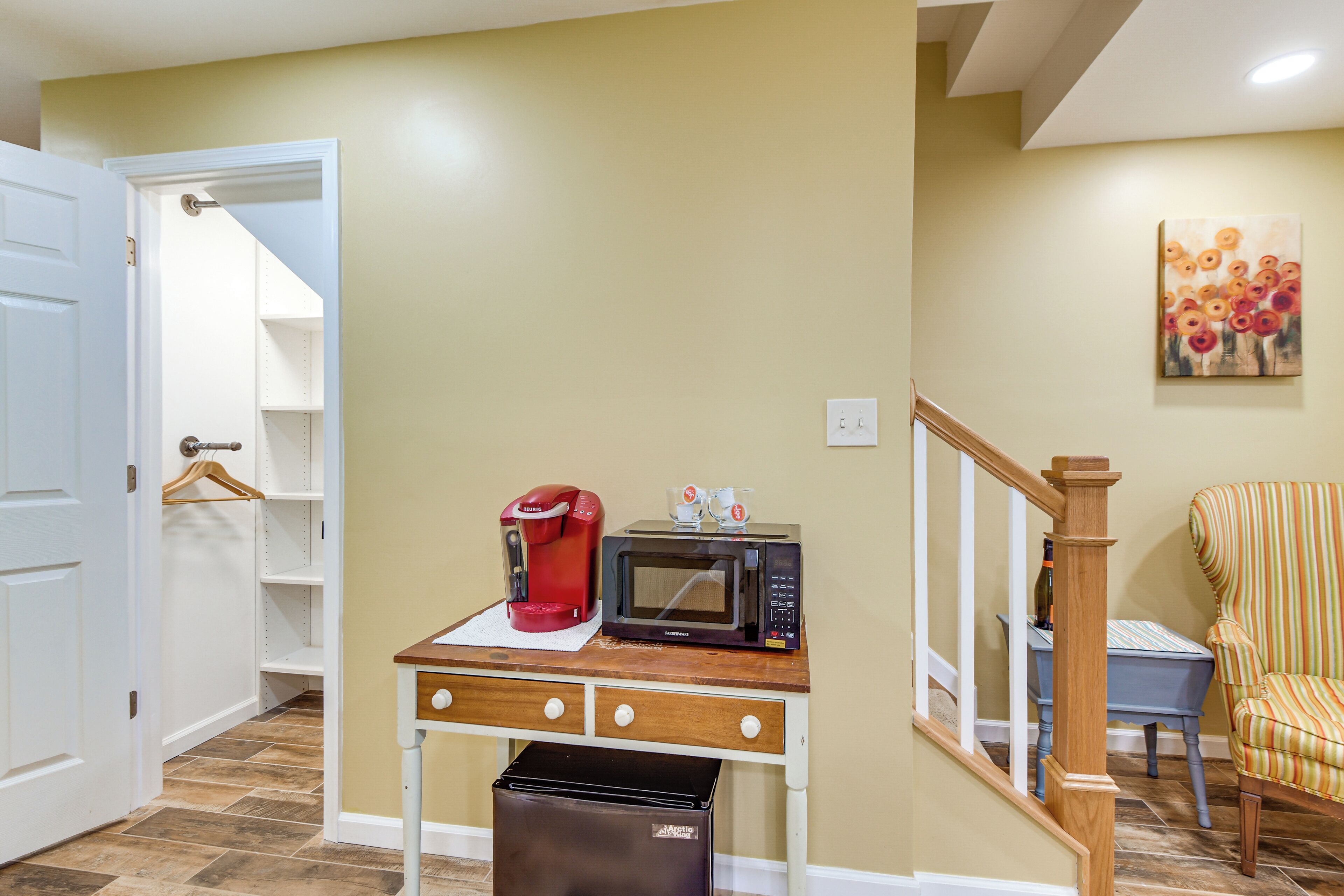A kitchenette with a coffee maker, microwave, and trash bin on a wooden table.