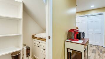 A compact kitchen with a built-in coffee maker, a trash can, and a small cabinet.