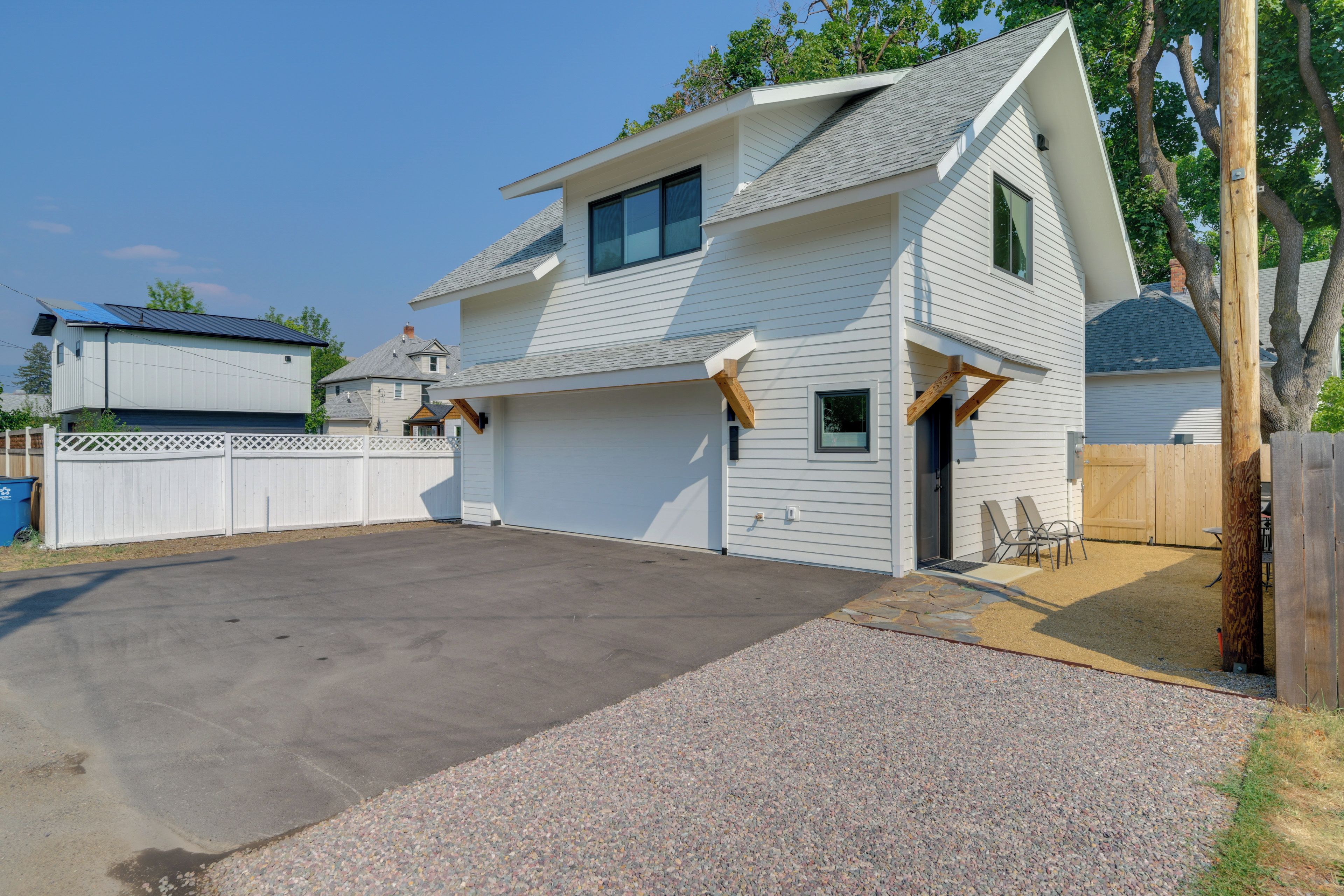 A two-story house with a garage, a fenced yard, and a gravel driveway.