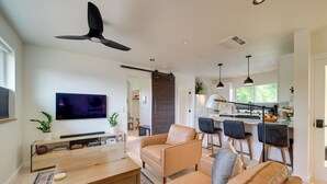 A modern living room with a flat-screen TV, leather sofas, a coffee table, and a ceiling fan.