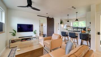 A modern living room with a flat-screen TV, leather sofas, a coffee table, and a ceiling fan.
