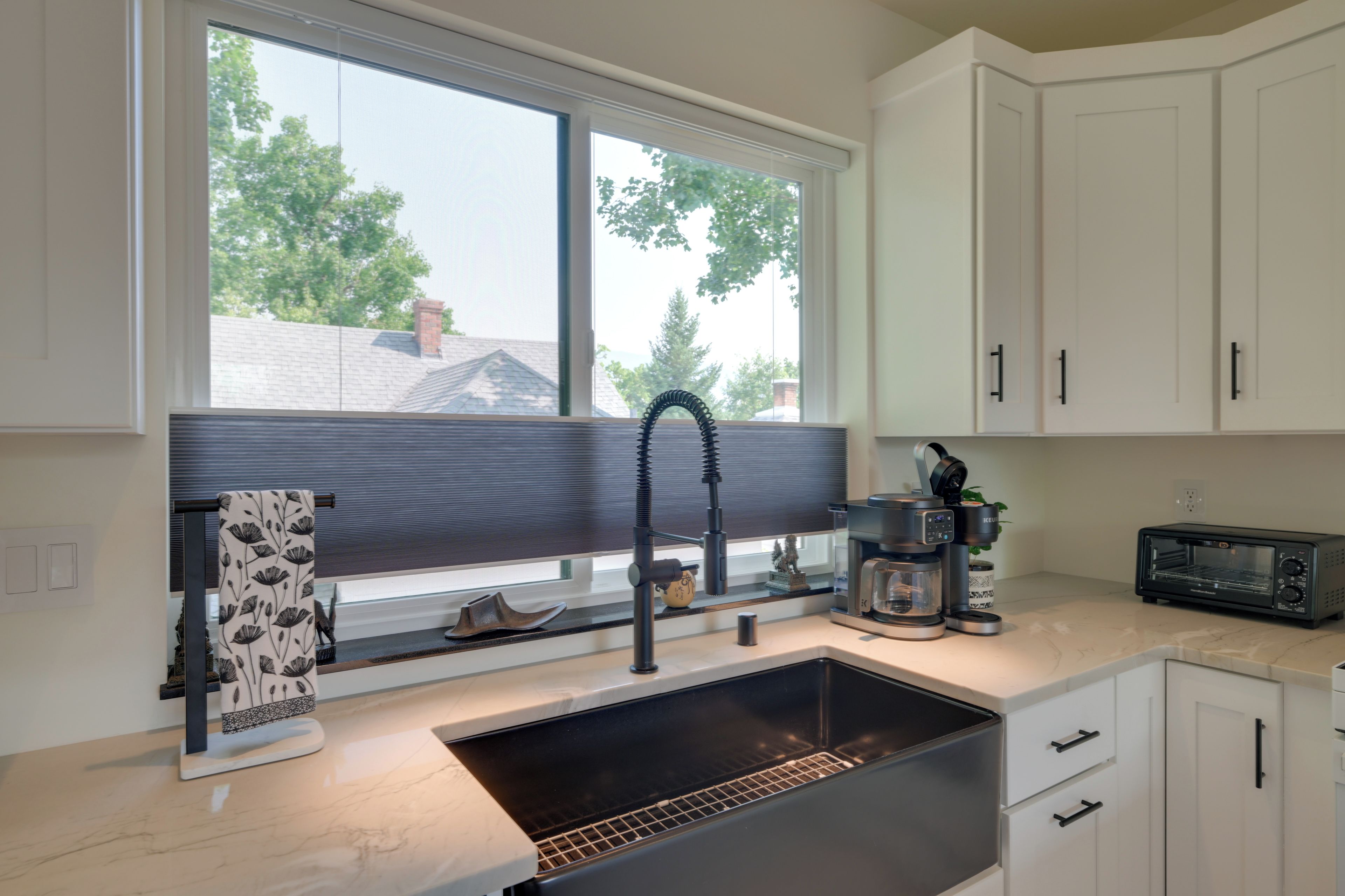 A kitchen with a large window, a sink, a coffee maker, and a toaster.