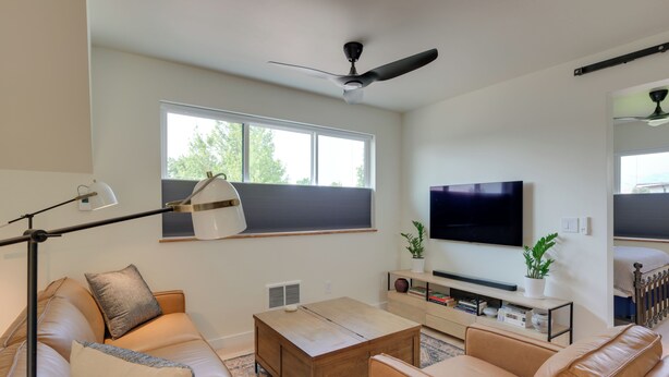 A modern living room with a sofa, coffee table, TV, and a ceiling fan.