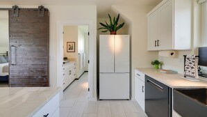 A modern kitchen with white cabinets, a built-in refrigerator, and a wooden accent wall.