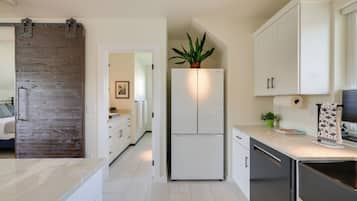 A modern kitchen with white cabinets, a built-in refrigerator, and a wooden accent wall.