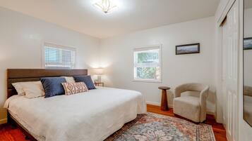 A bedroom with a bed, a chair, a rug, and two windows with blinds.