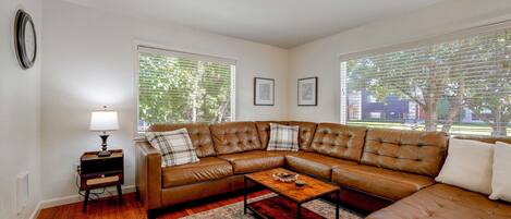 A living room with a brown leather sectional sofa, a wooden coffee table, a patterned rug, and a wall-mounted clock.