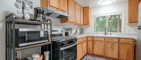 Una cocina moderna con armarios de madera, microondas integrado, estufa y ventana con persianas.