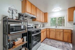 Una cocina moderna con armarios de madera, microondas integrado, estufa y ventana con persianas.