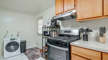 A compact kitchen with a washing machine, oven, microwave, and wooden cabinets.