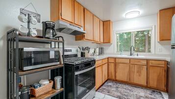 A modern kitchen with wooden cabinets, a built-in microwave, a stove, and a window with blinds.