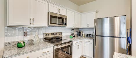 A modern kitchen with white cabinetry, stainless steel appliances, and a granite countertop.