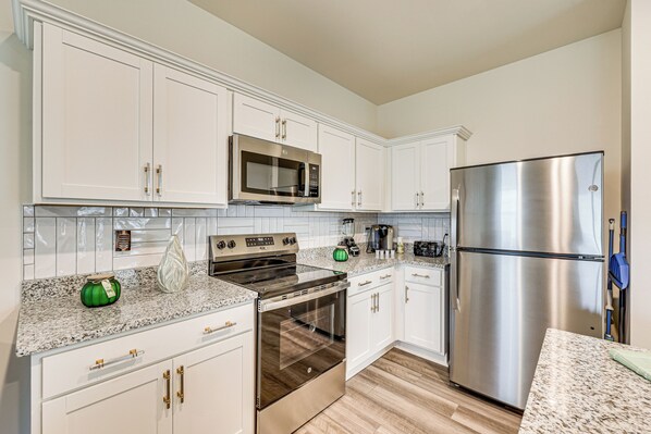 A modern kitchen with white cabinetry, stainless steel appliances, and a granite countertop.