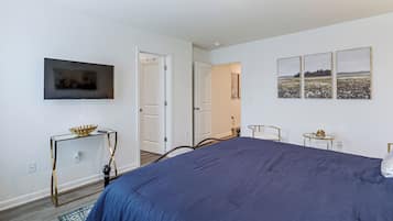 Un dormitorio con una cama grande, un televisor montado en la pared y una puerta que da a otra habitación.