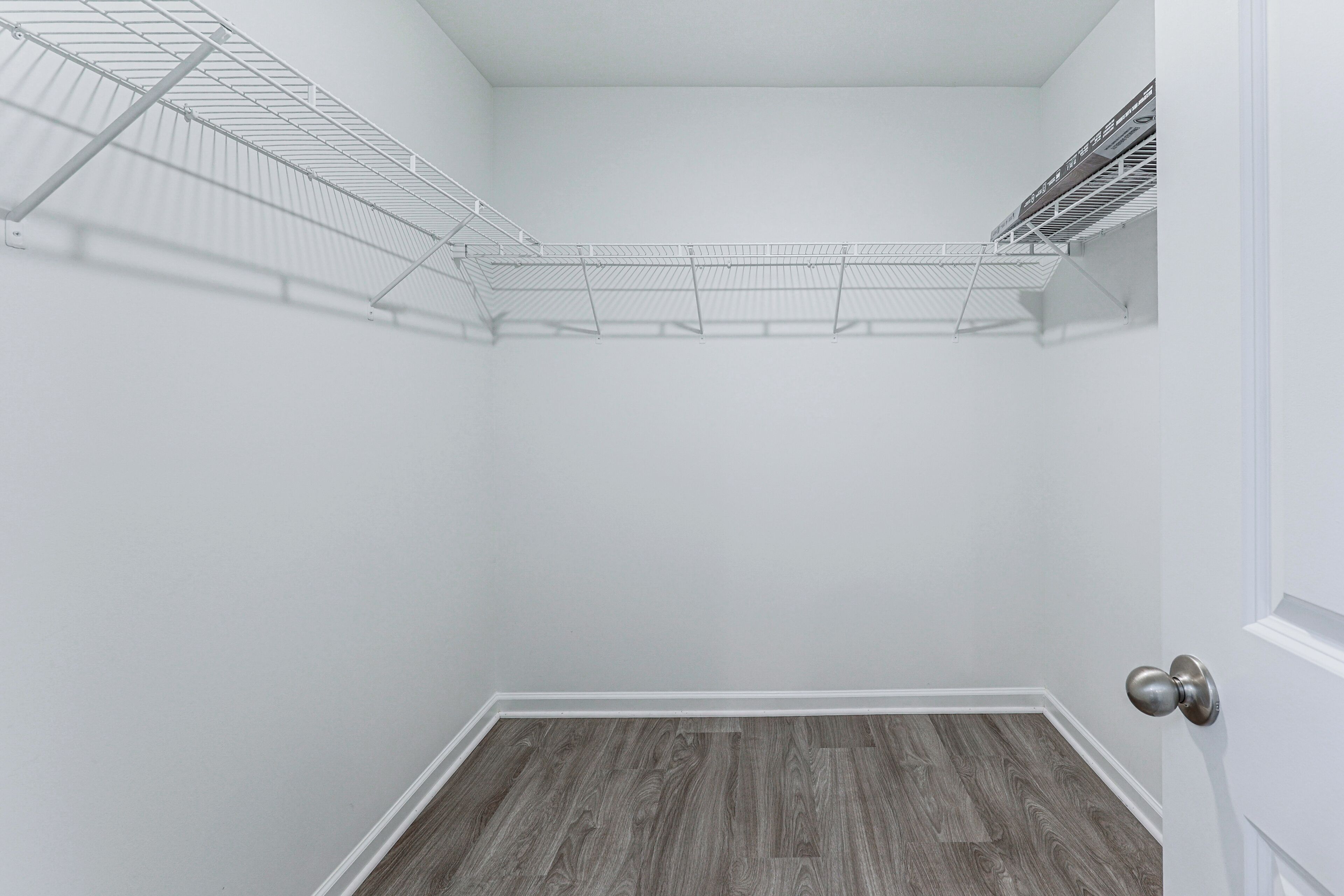 Un espacio de almacenamiento pequeño y cerrado con un estante metálico y suelo de madera.