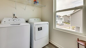A laundry room with two front-loading washing machines, a drying rack above, and a window with a view of a residential area.