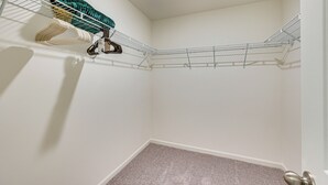 A corner of a room with a metal wire shelf holding various items, a carpeted floor, and a door with a silver handle.