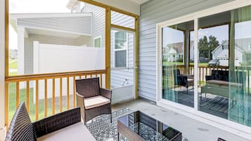 A covered patio with wicker furniture, a glass door leading outside, and a view of a residential neighborhood.
