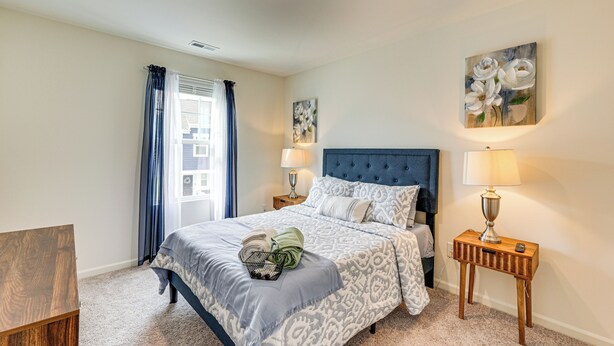 A bedroom with a large bed, two bedside tables with lamps, a window with curtains, and a painting on the wall.