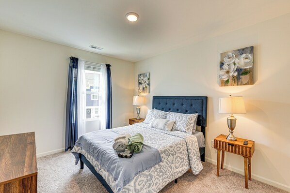 A bedroom with a large bed, two bedside tables with lamps, a window with curtains, and a painting on the wall.