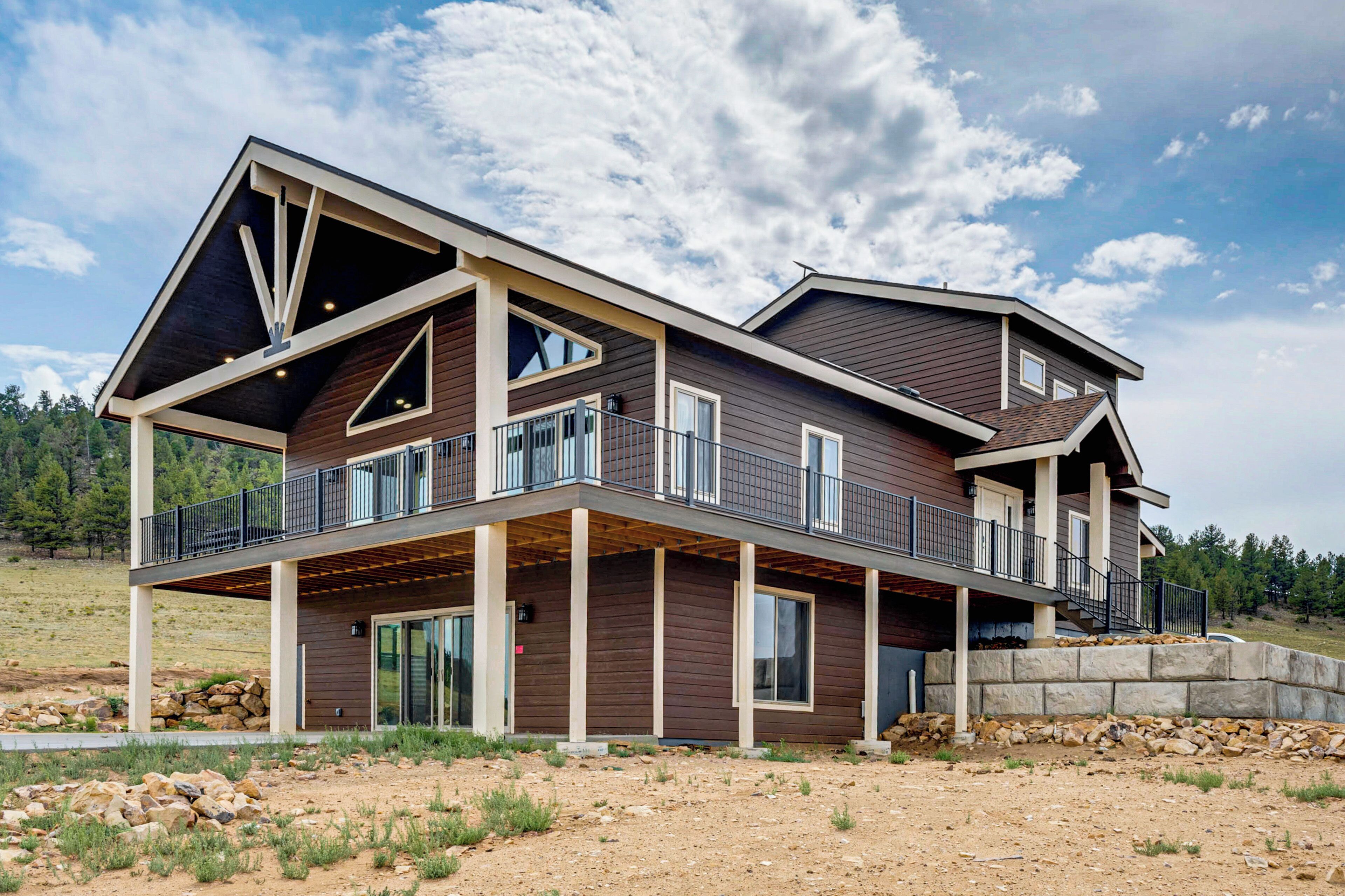 A modern two-story house with a balcony, large windows, and a stone foundation.