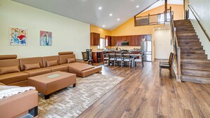 A spacious living area with a sectional sofa, a dining table with chairs, a kitchen with wooden cabinets, and a staircase leading to an upper level. - Mtn-view Deck! Remote South Park Retreat (Hartsel)