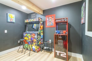 Ein Raum mit zwei Spielautomaten, einer mit der Aufschrift 'Arcade Classics' und der andere mit 'Terminator Judgment Day', sowie einem kleinen Tisch und Hockstühlen.
