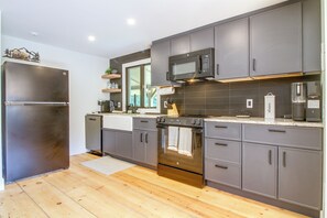 A modern kitchen with stainless steel appliances, grey cabinetry, and a wooden floor.