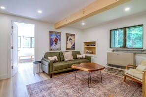 Ein Wohnzimmer mit einem grünen Sofa, einem Holztisch, einem gemusterten Teppich und einer Heizung.
