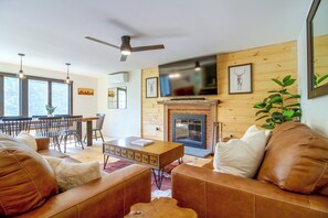 Ein Wohnzimmer mit Kamin, Ledersofas, einem Essbereich mit Stühlen und einem Fernseher, der über dem Kamin angebracht ist.