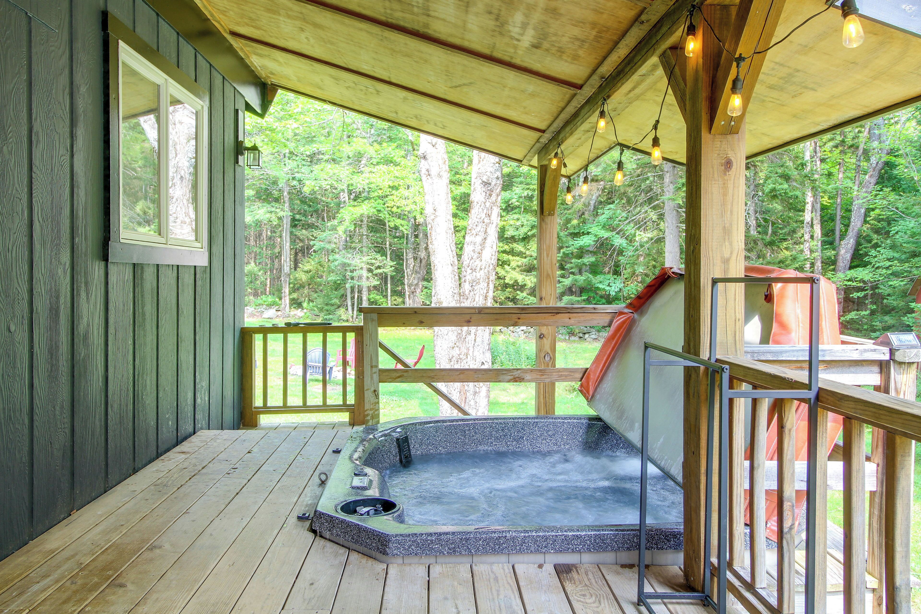 A wooden deck with a hot tub, a wooden railing, and a view of a forest.