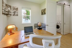 A room with a wooden desk, a laptop, a globe, a lamp, and a washing machine.