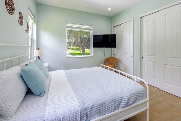 A bedroom with a bed, a television mounted on the wall, and a window with a view of trees.